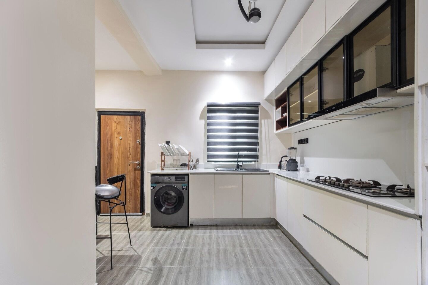 A compact kitchen with a washing machine, a sink, a stove, and a window with blinds.
