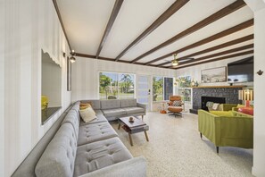 Ein Wohnzimmer mit einer Couch, Sesseln, einem Couchtisch, einem Kamin und einem Fernseher.