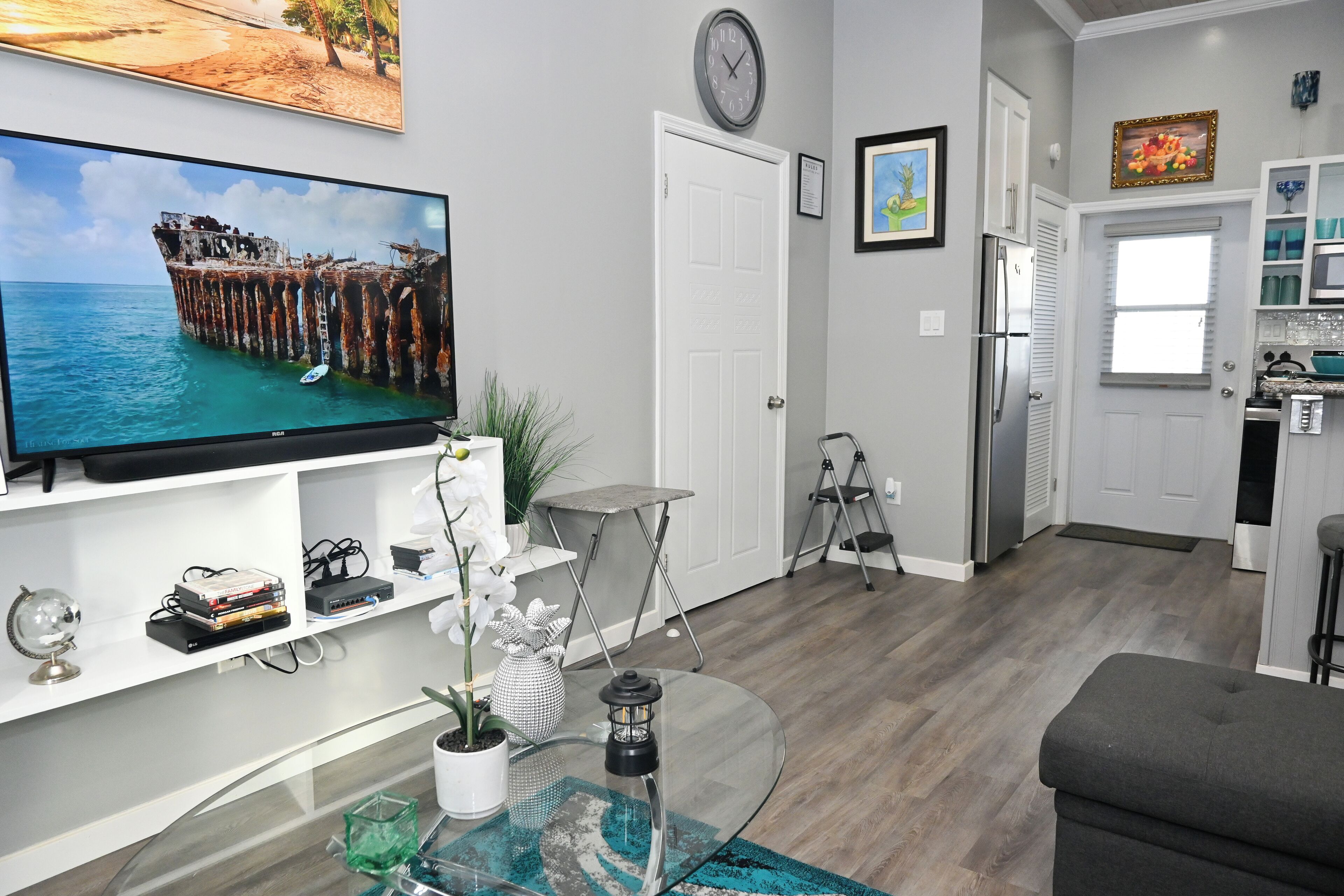 A modern living room with a TV, a glass coffee table, and a grey sofa.