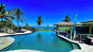 A swimming pool with lounge chairs, palm trees, and a view of the ocean. - Cute as a Button, AC, Starlink, Wi-Fi, Hot Tub, Near Beaches, Bars & Restaurants (North Palmetto Point)