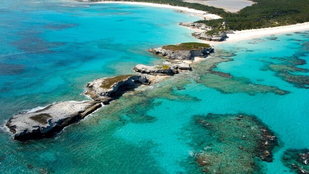 An aerial view of a coastal area with clear turquoise waters, rocky formations, and a sandy beach. - Cute as a Button, AC, Starlink, Wi-Fi, Hot Tub, Near Beaches, Bars & Restaurants (North Palmetto Point)