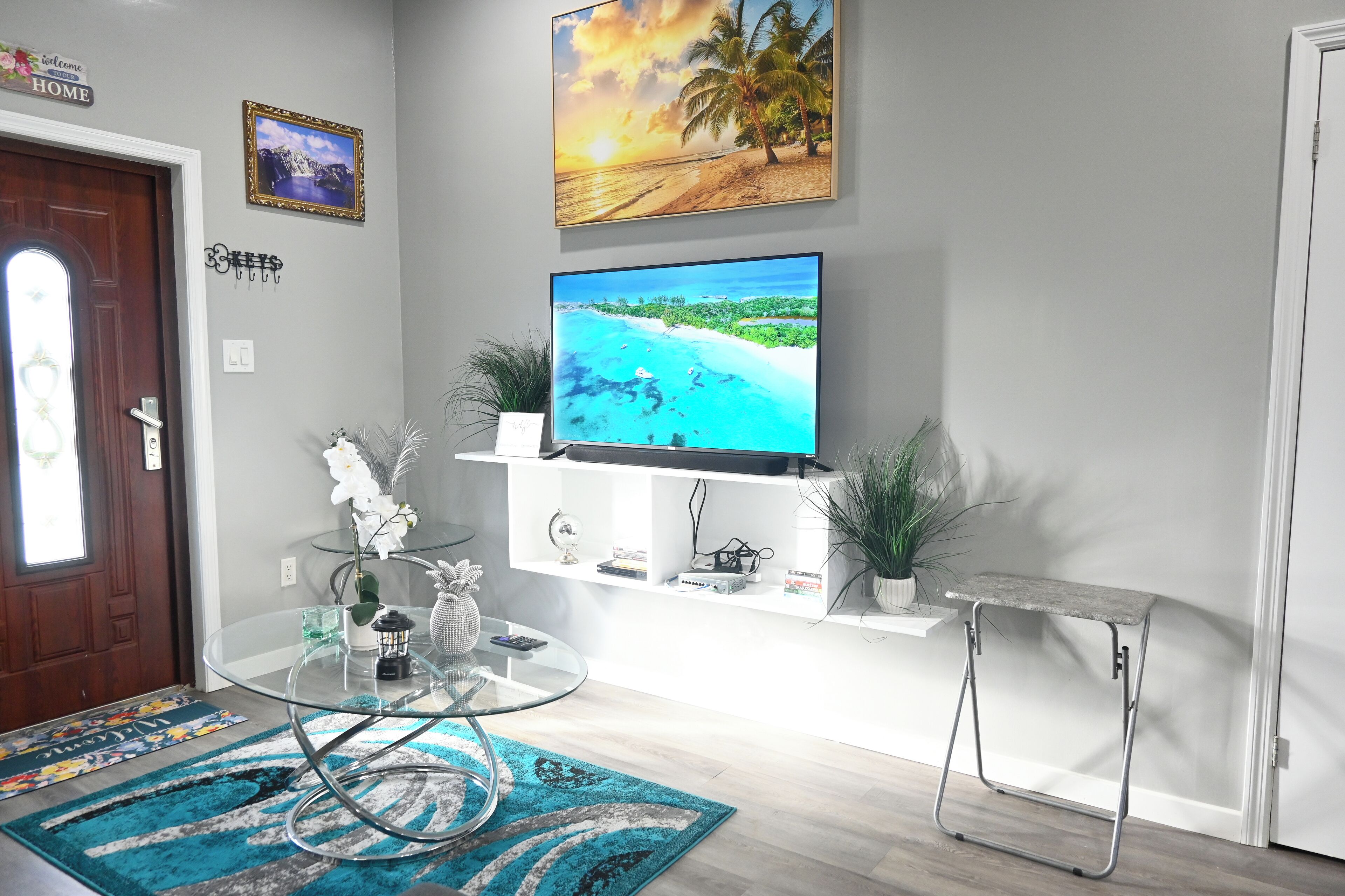 Una sala de estar moderna con televisor de pantalla plana, una mesa de centro de vidrio y una mesita auxiliar.