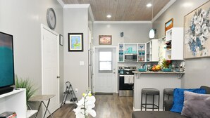 A modern living room with a sofa, TV, and a dining area with bar stools. - Cute as a Button, AC, Starlink, Wi-Fi, Hot Tub, Near Beaches, Bars & Restaurants (North Palmetto Point)