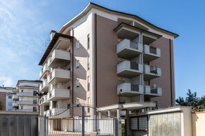 A multi-story residential building with balconies, a gated entrance, and a clear sky.