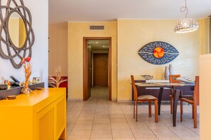 A hotel lobby with a reception desk, a dining area with a table and chairs, a decorative wall art piece, and a door leading to another room.
