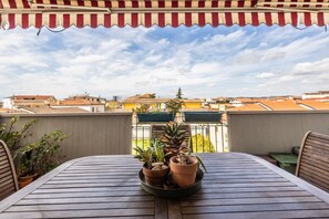 A wooden table with potted plants, a striped awning, and a view of buildings in the background.