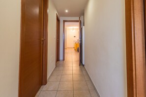Un corridoio con porte in legno, pavimento piastrellato e un oggetto giallo in lontananza.