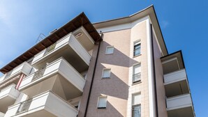 Ein mehrgeschossiges Wohngebäude mit Balkonen, einer flachen Dachterrasse und blauem Himmel.
