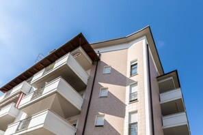 Un edificio residenziale a più piani con balconi, un tetto piatto e un cielo azzurro.