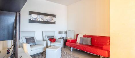 A modern living room with a red sofa, two armchairs, a coffee table, and a TV.