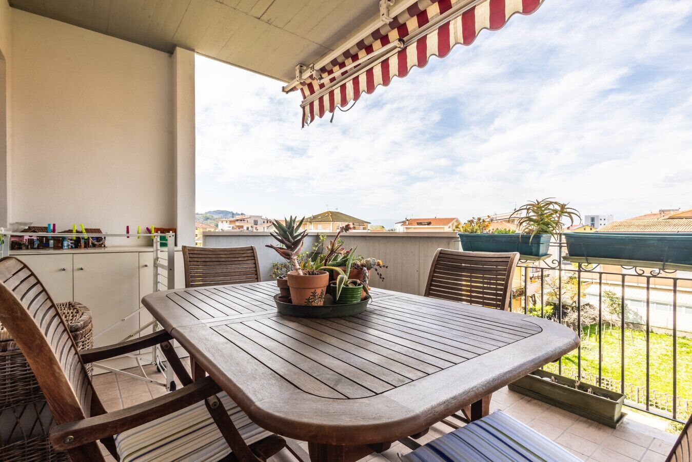 A balcony with a wooden table and chairs, potted plants, and a view of buildings.