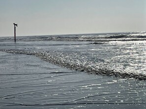 Ein Strand mit einem Steg, der sich ins Wasser erstreckt, Wellen, die an das Ufer schlagen, und einem klaren Himmel.