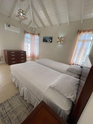 Ein Schlafzimmer mit zwei Betten, einem Schminktisch, einem Fenster mit Vorhängen und einem Deckenventilator.