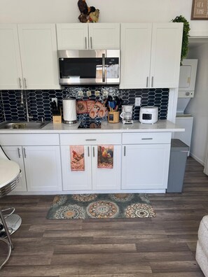 A kitchen with white cabinets, a stainless steel microwave, a coffee maker, and a patterned backsplash. - Tranquil stay Vegas (Las Vegas)