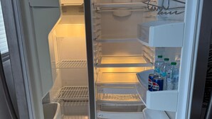 An open refrigerator with multiple shelves, a water filter, and a 'HELLO' mat on the floor. - Tranquil stay Vegas (Las Vegas)