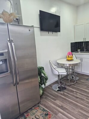 A compact kitchen with a stainless steel refrigerator, a small dining table with a chair, a flat-screen TV mounted on the wall, and a potted plant. - Tranquil stay Vegas (Las Vegas)
