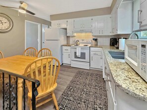 Une cuisine moderne avec des meubles blancs, un four encastré, un micro-ondes et un coin repas comprenant une table et des chaises en bois.