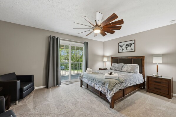 Une chambre à coucher comprenant un lit, une table de chevet, une chaise, un ventilateur de plafond et une fenêtre avec des rideaux.