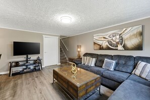 Ein Wohnzimmer mit Flachbildfernseher, Couch, Couchtisch und einem Bild an der Wand.