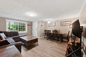 Ein Wohnzimmer mit Sofa, Couchtisch, Fernseher und einem Essbereich mit Stühlen und Tisch.
