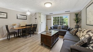 Ein Wohnzimmer mit einer Couch, einem Esstisch mit Stühlen, einem Couchtisch und einer Deckenleuchte.