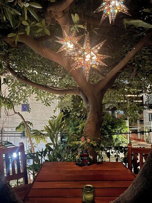 Un arbre amb llums penjants en forma d'estrelles, una banca de fusta i una petita estàtua.