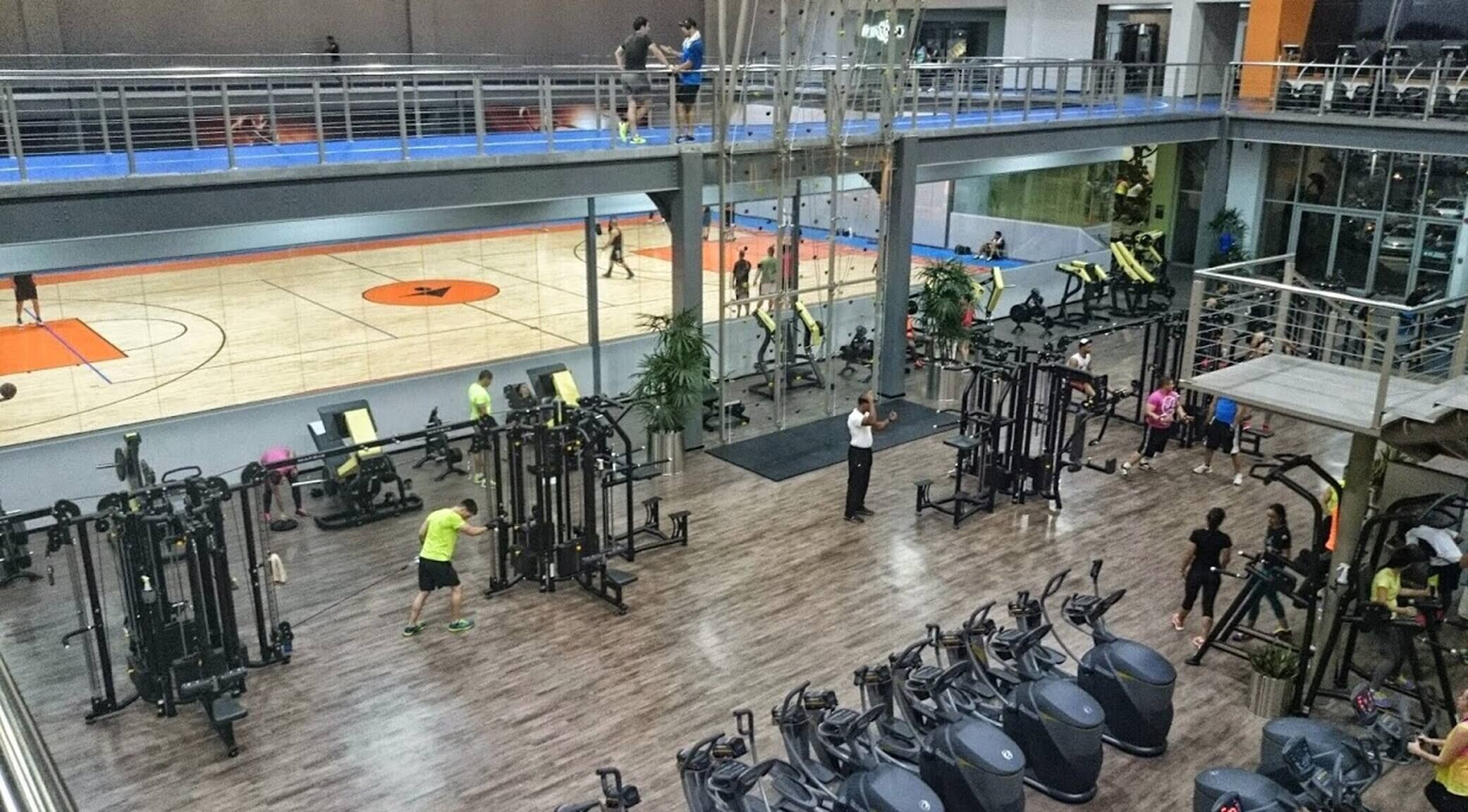 Un gimnasio de varios niveles con diferentes equipos de ejercicio, una cancha de baloncesto y una zona de descanso.
