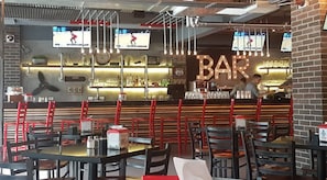 Un bar con mostrador, sillas rojas y una pantalla mostrando deportes.
