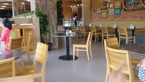 Interior de restaurante con sillas y mesas de madera, una barra con una persona atendiendo y una pared decorada con diversos objetos, incluyendo una bicicleta.