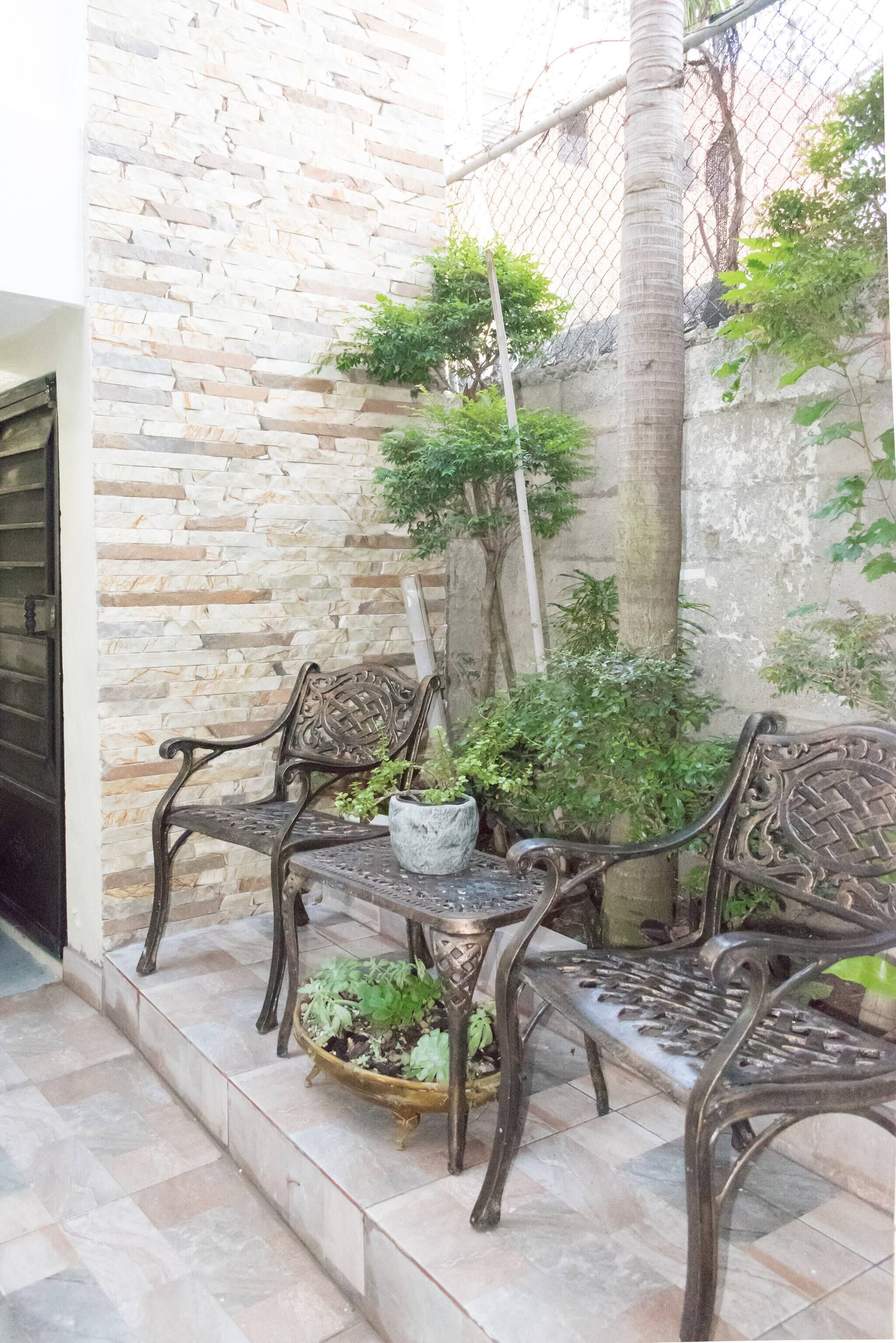 A courtyard with a stone wall, a metal bench, a table, and potted plants.