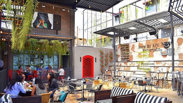 Un espacio al aire libre con mesas y sillas, una puerta roja y una pared con un letrero.