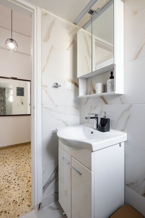 Ein Badezimmer mit einem weißen Waschbecken, einem Spiegel und Marmorwänden.