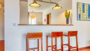 A dining area with a large mirror, three wooden chairs, two pendant lights, and a vase with flowers on a shelf. - Verde Água Garajau, a Home in Madeira (Santa Cruz)