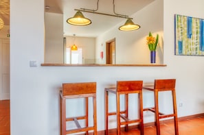 A dining area with a large mirror, three wooden chairs, two pendant lights, and a vase with flowers on a shelf. - Verde Água Garajau, a Home in Madeira (Santa Cruz)