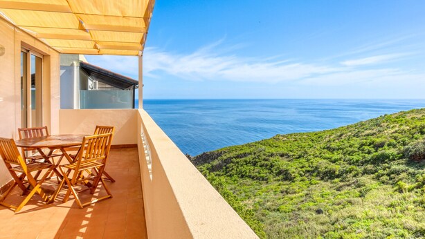 A balcony with a table and chairs, overlooking a coastal landscape. - Verde Água Garajau, a Home in Madeira (Santa Cruz)