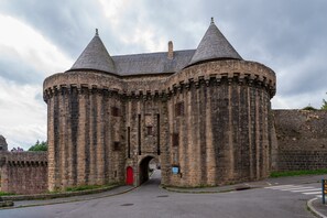 A historic stone castle with a central archway, crenellated walls, and a red door.