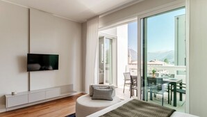 Una habitación de hotel moderna con una cama grande, un televisor de pantalla plana, un balcón con zona de comedor y vistas a las montañas.