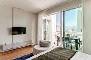 Ein modernes Hotelzimmer mit einem großen Bett, einem Flachbildfernseher, einem Balkon mit Essbereich und Blick auf Berge.