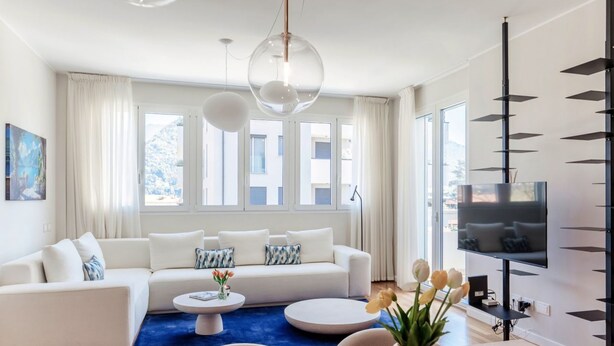 Una sala de estar moderna con un sofá blanco, una mesa de centro redonda y un televisor sobre un mueble negro.