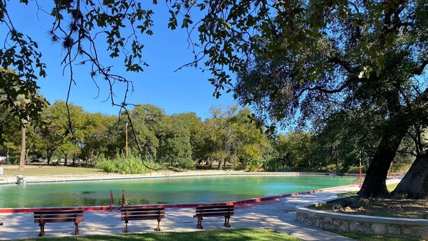 Um parque com piscina, bancos e árvores.