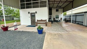 Área externa coberta com um banco, plantas em vasos e uma porta para um edifício.