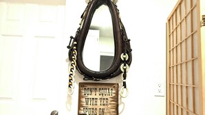 Um espelho com moldura decorativa, uma placa abaixo e uma cesta de vime sobre uma mesa de madeira.