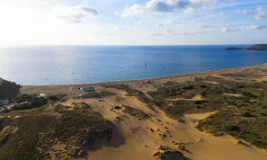 Eine Luftaufnahme einer Küstenlandschaft mit Strand, vereinzelter Vegetation und blauem Himmel.