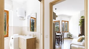 Ein modernes Badezimmer mit integrierter Waschmaschine, einem großen Spiegel und einem Fenster.