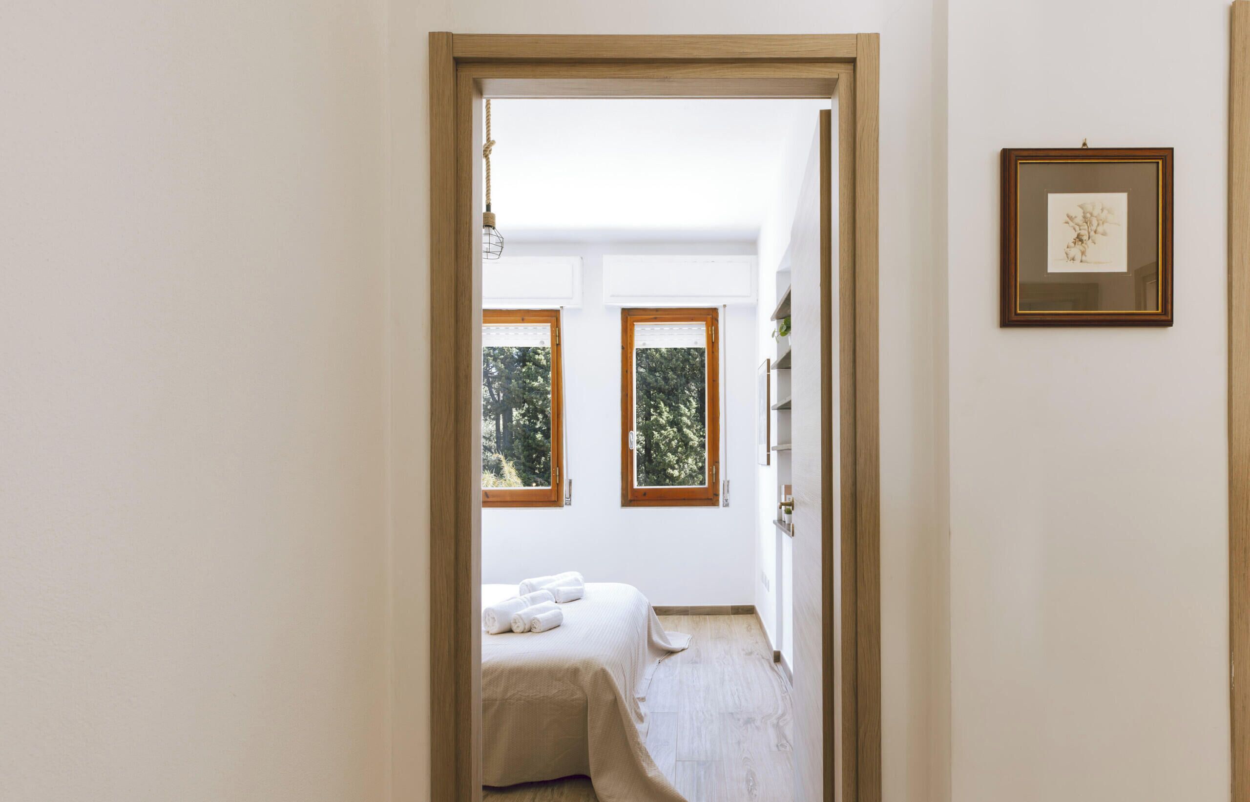 A bedroom with a bed, two windows, a framed picture, and a wooden door.