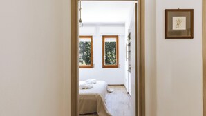 Ein Schlafzimmer mit einem Bett, zwei Fenstern, einem gerahmten Bild und einer Holztür.