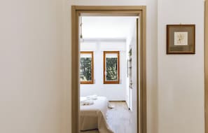 Ein Schlafzimmer mit einem Bett, zwei Fenstern, einem gerahmten Bild und einer Holztür.