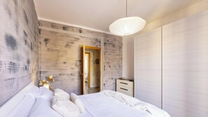 Un dormitorio con cama, mesita de noche, armario, lámpara colgante y puerta que da a otra habitación.