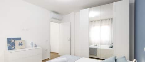 Une chambre à coucher comprenant un lit, une commode, une armoire et une salle de bain visible à travers une porte vitrée.