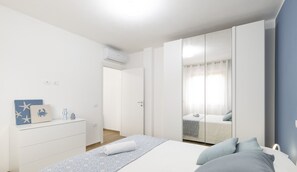 A bedroom with a bed, a dresser, a wardrobe, and a bathroom visible through a glass door. - Blue Modern Apartment (Monserrato)